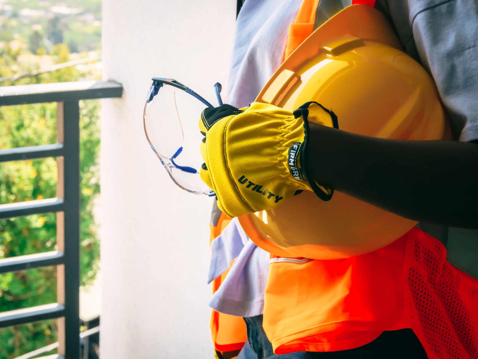 Werknemer met gele werkhandschoenen houdt een veiligheidsbril en een gele veiligheidshelm vast